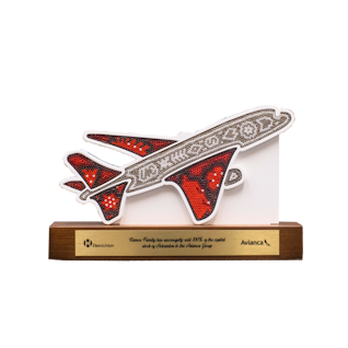 Trofeo de madera con forma de avión cubierto con chaquiras sobre base de madera