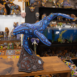 Escultura de ballena jorobada color azul sobre base color café cubierta con chaquiras