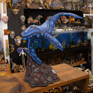 Escultura de ballena jorobada color azul sobre base color café cubierta con chaquiras
