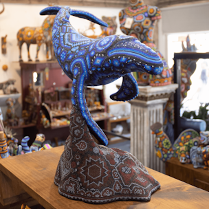 Escultura de ballena jorobada color azul sobre base color café cubierta con chaquiras